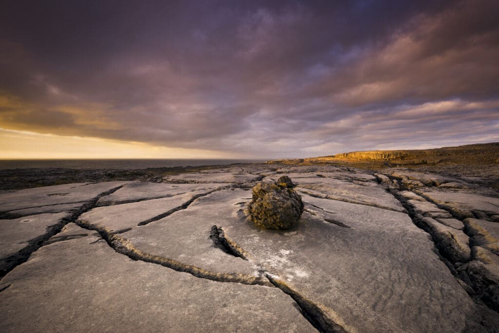 - A lonely boulder rests on cracked earth under a dramatic sunset sky.